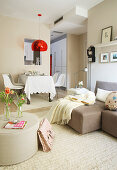 Shells chairs below transparent red lampshade in dining area with sofa set in foreground