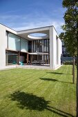 Modern architect-designed house with flat roof, glass façade, roofed terrace and manicured lawn
