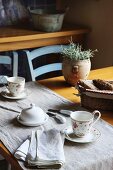 Table set for two with runner, floral teacups, white butter dish and basket of bread