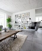 Rustic coffee table made from reclaimed wood and classic grey armchairs in front of open shelves in living room with grey tiled floor