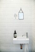 Sink below small mirror next to motto on white tiled wall