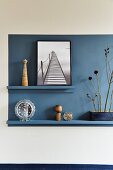 Blue rectangle on wall with ornaments on narrow blue shelves