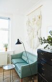 Pale wall hanging above turquoise two-seater sofa