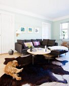 Wohnbereich mit schwarzer Couch, Tierfellteppich und Hund