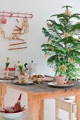 Christmas table decorated with hyacinths in vintage cups, stollen fruit cake, espresso pot, small Christmas tree with straw stars and garlands of dried apple slices against wall