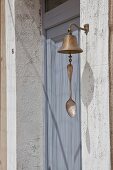 Bell with vintage spoon attached to clapper next to dove-grey front door