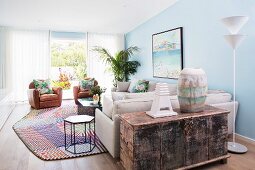 Light-flooded living room in a mix of styles with light blue walls, sofa, leather armchairs and antique wooden chest