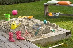 Sandkasten mit Spielzeug und Kinder - Gummistiefeln