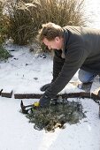 Mann schlägt Loch in zugefrorenen Teich