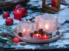 Windlichter - Eissterne auf Terracotta - Untersetzer mit Zapfen und roten Kerzen