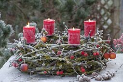Adventskranz aus bemoosten Zweigen auf Metallgestell mit Kerzenhaltern