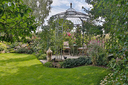 Round metal pavilion with small seating area, curved perennial beds with natural stones, pottery decorative elements
