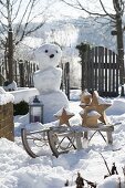 Snowy garden with snowman and sleigh with wooden stars