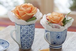 Einzelne Blüten von Rosa (Rosen) mit Tortenspitze in Tassen