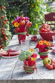 Feurige Tischdeko mit Gemüse und Sommerblumen in roten Bechern