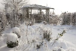 Pavilion in the snowy garden, flowerbeds with perennials