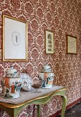 China pots with lids on green console table against ornate wallpaper