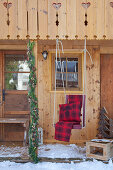 Schaukelstuhl mit roter Decke und Kissen hängt am Gartenhaus