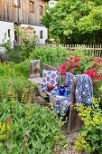 Crocheted blanket and cushions on wooden bench in idyllic cottage garden
