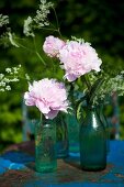 Various glass bottles filled with peonies and flowering chervil