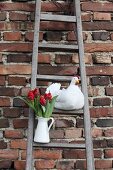 Hand-made fabric hen and white jug of red tulips on rustic wooden ladder