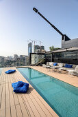 Long, narrow swimming pool and sofa combination on roof terrace with view of city