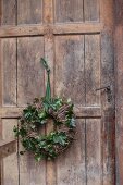 Weidenkranz mit grünen Efeuranken an rustikaler Holztür