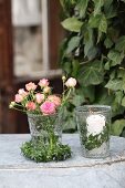 Romantic arrangement of ivy wreaths, roses and lit candle in glass vases