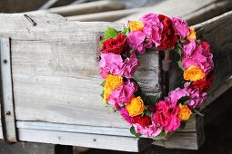 Wreath of hydrangeas and roses in shades of red and orange hung on corner of old wooden crate