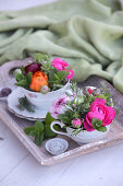 Colourful flower arrangements in old-fashioned teacups on vintage wooden tray