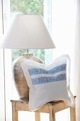 Cushion cover hand made from white linen and floral trim next to table lamp on wooden stool
