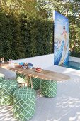 Surfboard table with green poufs in front of pool and mosaic