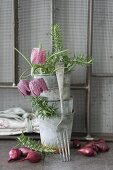 Vintage-style arrangement of stacked zinc pots, snake's head fritillaries, onions and fork