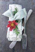 Linen napkin tied with rosemary sprig and flower next to vintage cutlery