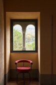 Chair with red upholstery in niche below Romanesque window with stone pillar