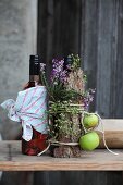 Herbstlich dekorierte Flasche, umwickelt mit Baumrinde, Heidekraut und festgebundenen grünen Äpfeln