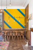 Yellow wall with diagonal stripes above dining table and wooden chairs