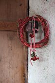 Weidenkranz mit Hagebuttensträußchen an rot-weißem Schleifenband aufgehängt vor Vintage Wand mit Holztür
