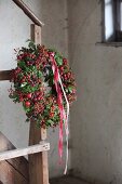 Autumn wreath of rose hips, moss and red and white ribbons on newel post of vintage wooden stairs