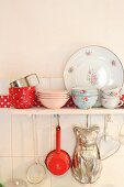 Romantic crockery on wall-mounted shelf with kitchen utensils hung from underside