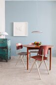 Dining area with retro table, chairs and modern pendant lamp against pale blue wall