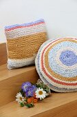 Flowers next to pastel cushions with crocheted covers made from T-shirt yarn