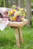 Vase of colourful wildflowers on vintage wooden stool in garden