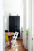 High chair at wooden table next to window and black wall-mounted cabinet in dining area