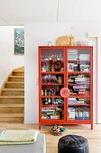 Games, glasses and magazines in red, glass-fronted cabinet next to foot of staircase