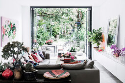 Leather furniture, console table and lowboard with house plants in the living room, view of the green terrace