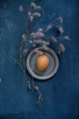 Egg on pewter plate and dried twigs on blue surface
