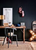Rustic desk with brass table lamp, New York map, radio, coffee pot and hat against black wall with boxing gloves