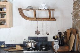 Kitchen utensils hung from old wooden sledge mounted on wall in kitchen