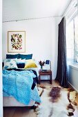 Blue knitted bedspread on double bed and animal fur rug in bedroom